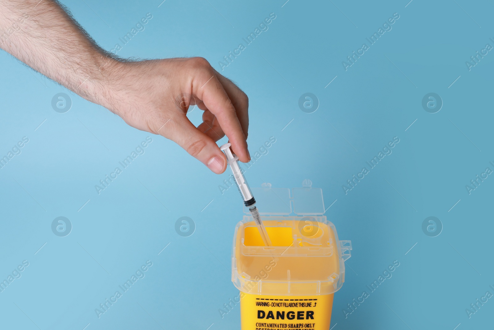 Photo of Man throwing used syringe into sharps container on light blue background, closeup