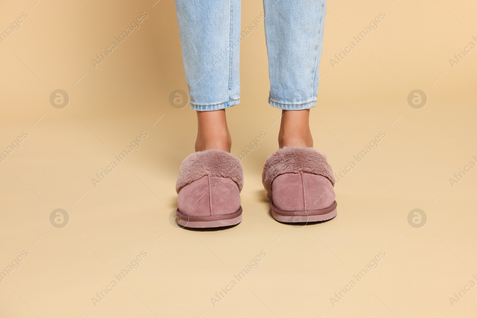 Photo of Woman in warm soft slippers on beige background, closeup