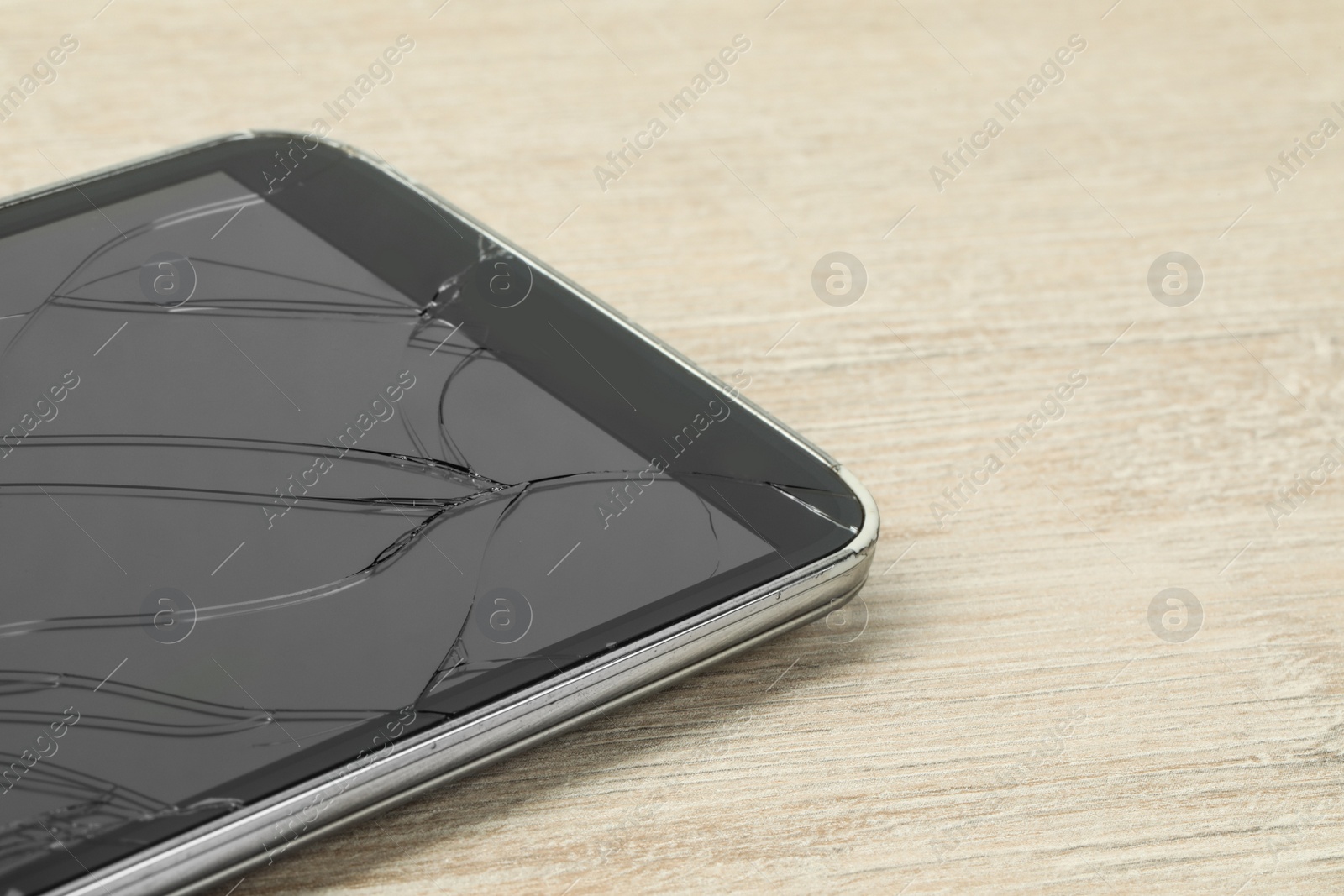 Photo of Smartphone with cracked screen on light beige wooden background, closeup. Device repair