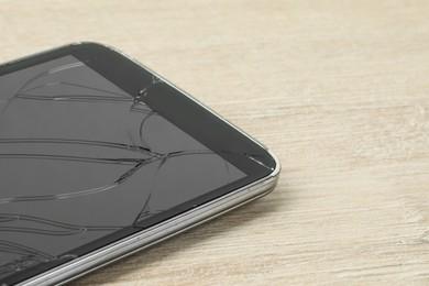 Photo of Smartphone with cracked screen on light beige wooden background, closeup. Device repair