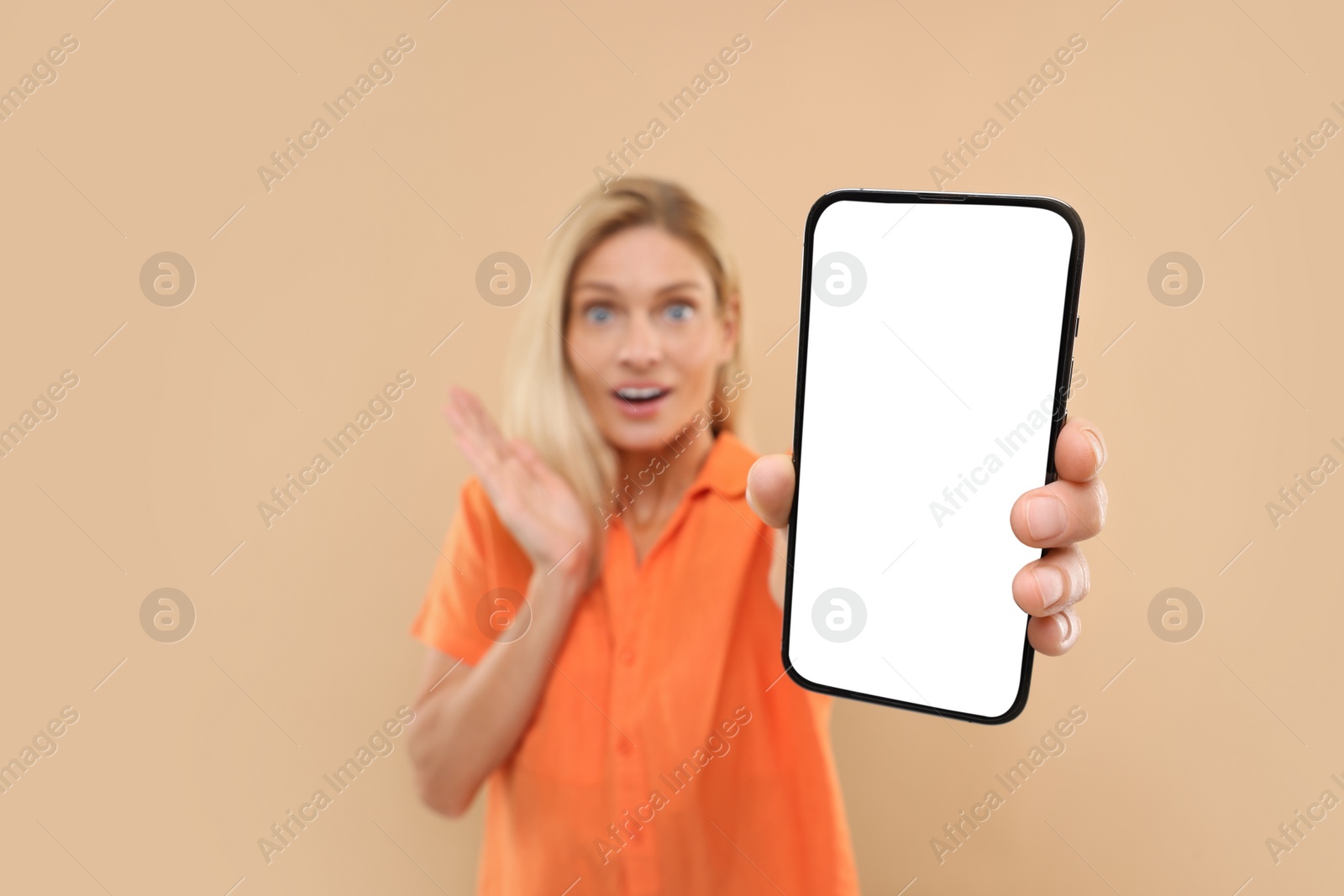 Photo of Surprised woman holding smartphone with blank screen on beige background, selective focus