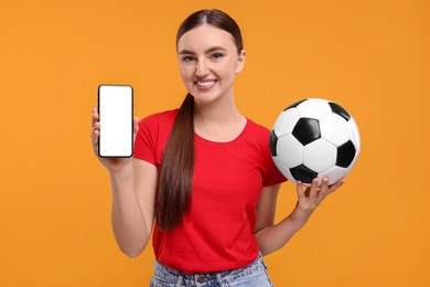 Photo of Happy soccer fan with ball showing smartphone on orange background