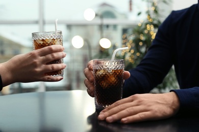 Couple with glasses of cold cola at table in cafe, closeup