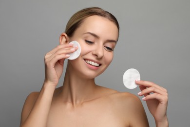 Smiling woman removing makeup with cotton pads on grey background