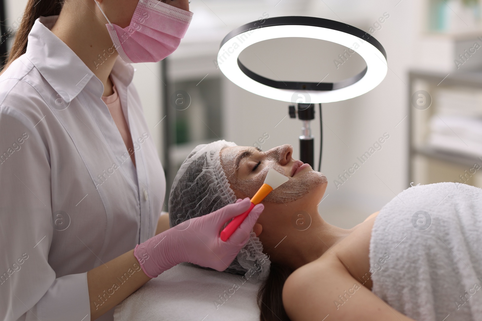 Photo of Cosmetologist applying mask on woman's face in clinic, closeup