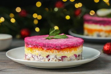 Photo of Herring under fur coat salad on white wooden table against blurred festive lights, closeup with space for text. Traditional Russian dish