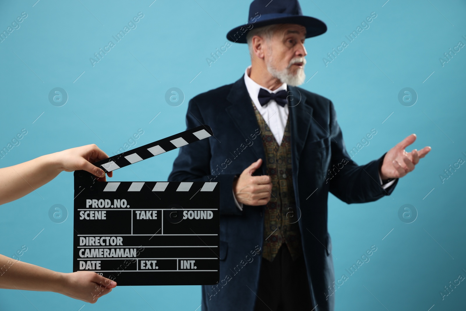 Photo of Senior actor performing role while second assistant camera holding clapperboard on light blue background, selective focus. Film industry