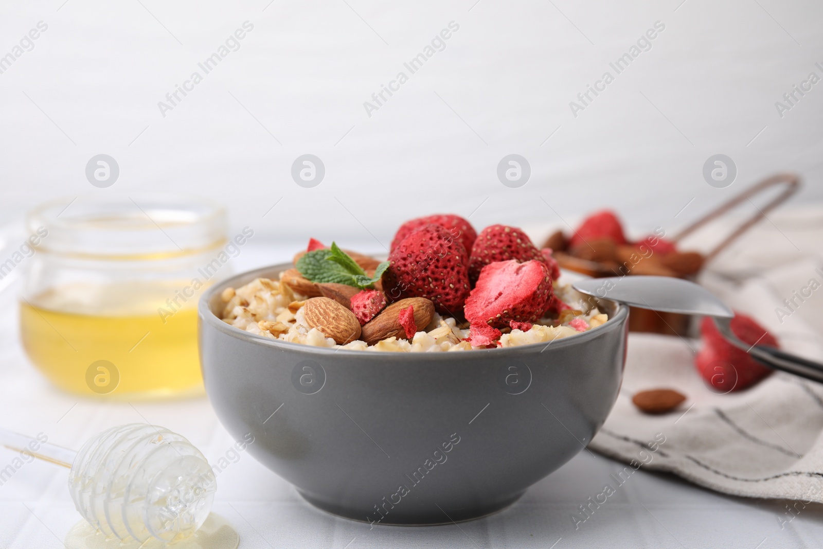 Photo of Delicious oatmeal with freeze dried strawberries, almonds and mint on white table, closeup