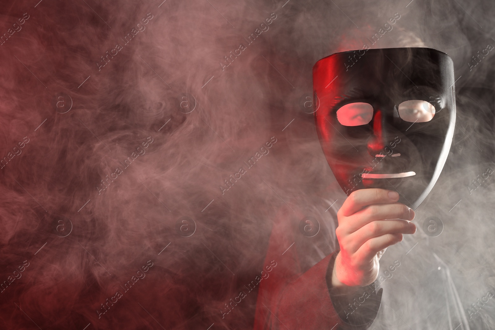 Photo of Theatrical performance. Man with plastic mask in smoke on dark background, space for text