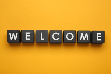 Photo of Word Welcome made of black cubes on yellow background, top view