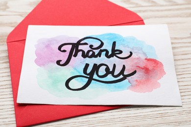 Photo of Envelope and card with phrase Thank You on light wooden table, closeup