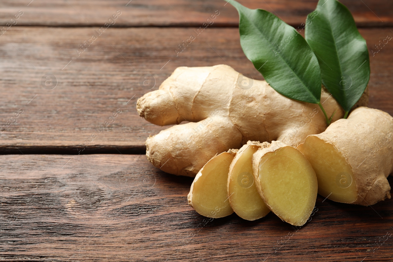 Photo of Cut and whole fresh ginger with leaves on wooden table, closeup. Space for text