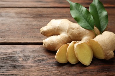 Cut and whole fresh ginger with leaves on wooden table, closeup. Space for text