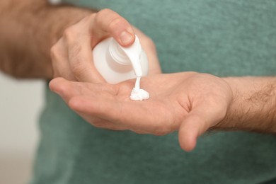 Photo of Man applying cream from dispenser onto hand on light grey background, closeup