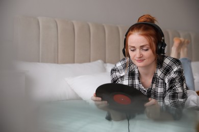 Young woman listening to music with turntable in bedroom. Space for text