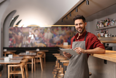 Photo of Young male business owner with tablet near counter in his cafe. Space for text