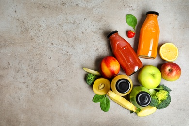 Photo of Bottles of delicious juices and fresh fruits on grey table, flat lay. Space for text