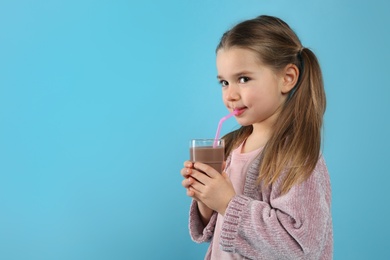 Cute little child drinking tasty chocolate milk on light blue background, space for text