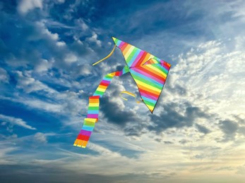 Image of Bright striped rainbow kite flying in blue sky