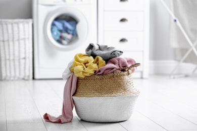 Photo of Wicker basket with dirty laundry on floor indoors