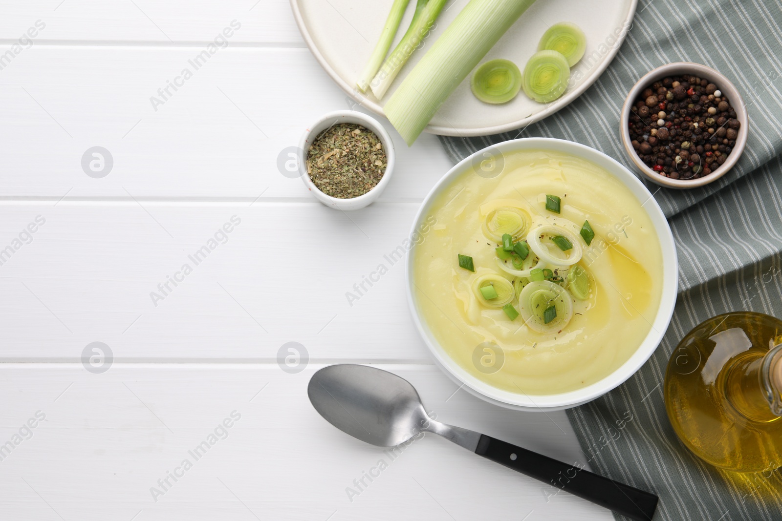 Photo of Bowl of tasty cream soup with leek and spoon on white wooden table, flat lay. Space for text
