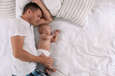 Father and baby sleeping on bed together, top view. Space for text