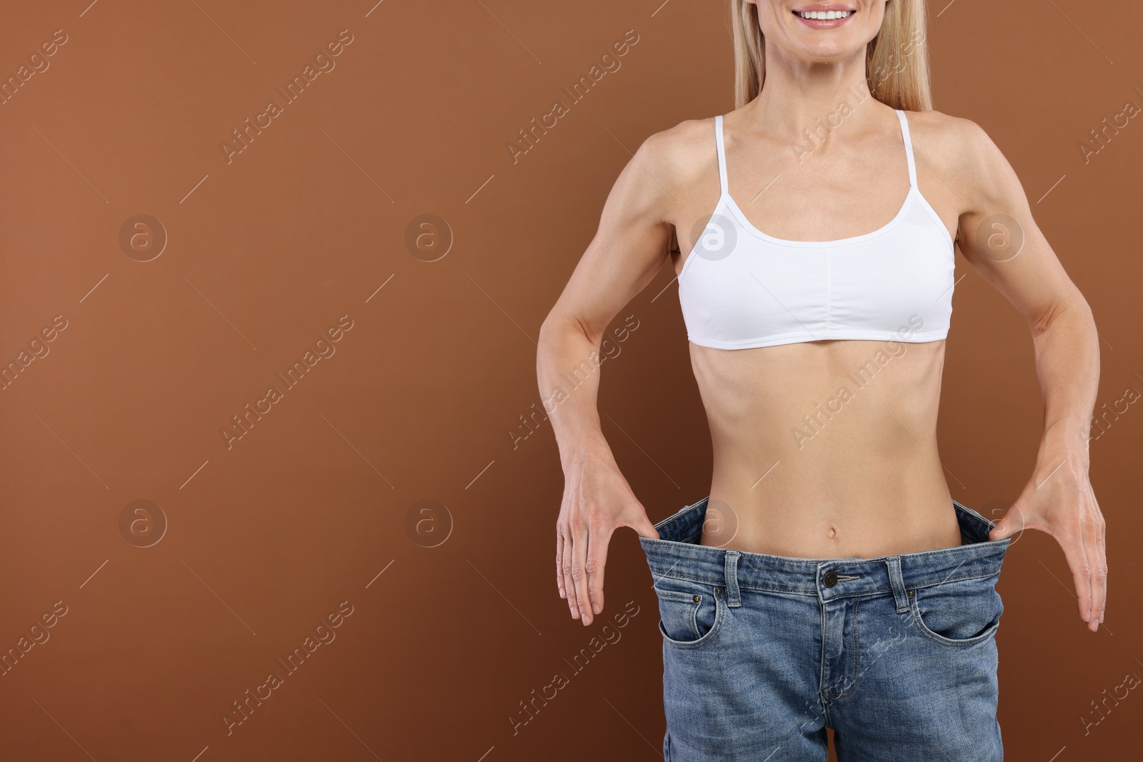 Photo of Slim woman wearing big jeans on brown background, closeup and space for text. Weight loss