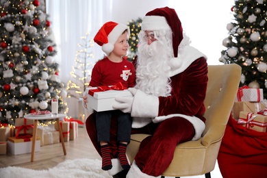 Santa Claus giving present to little boy in room decorated for Christmas