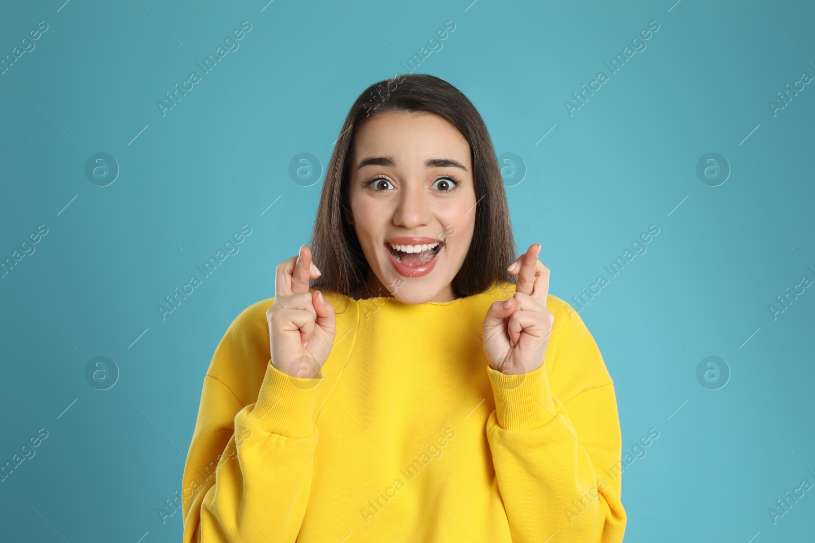 Photo of Woman with crossed fingers on light blue background. Superstition concept