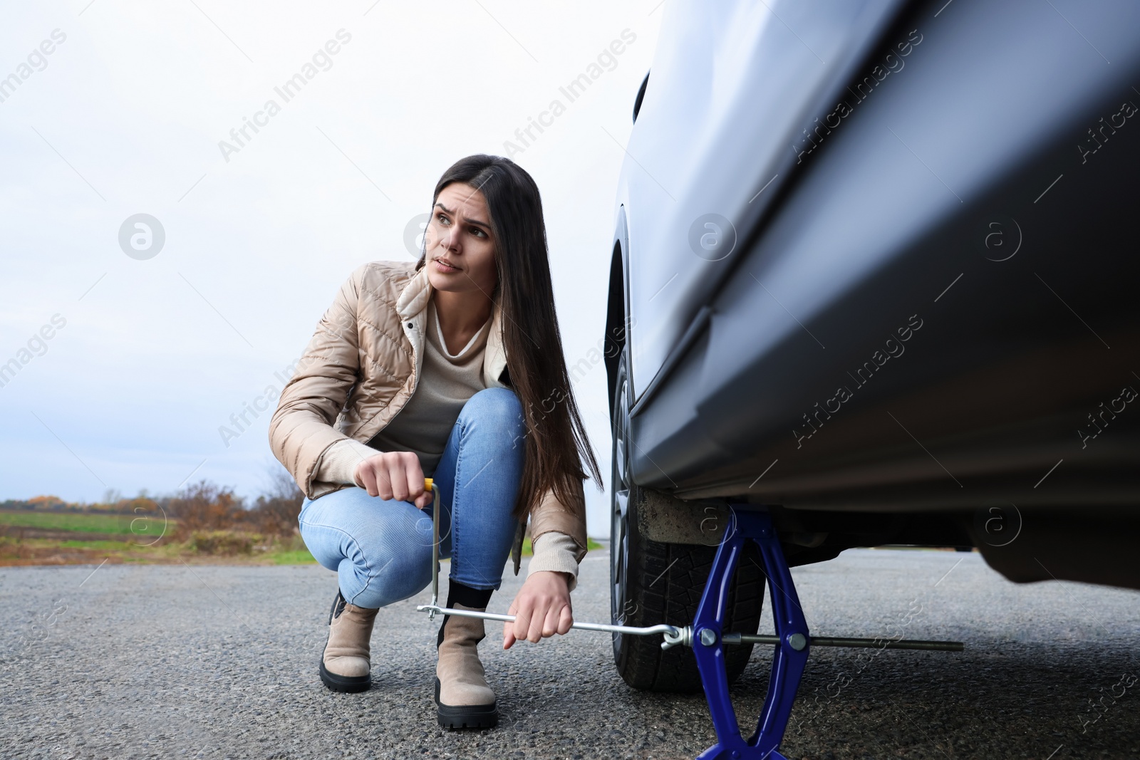 Photo of Young woman changing tire of car on roadside