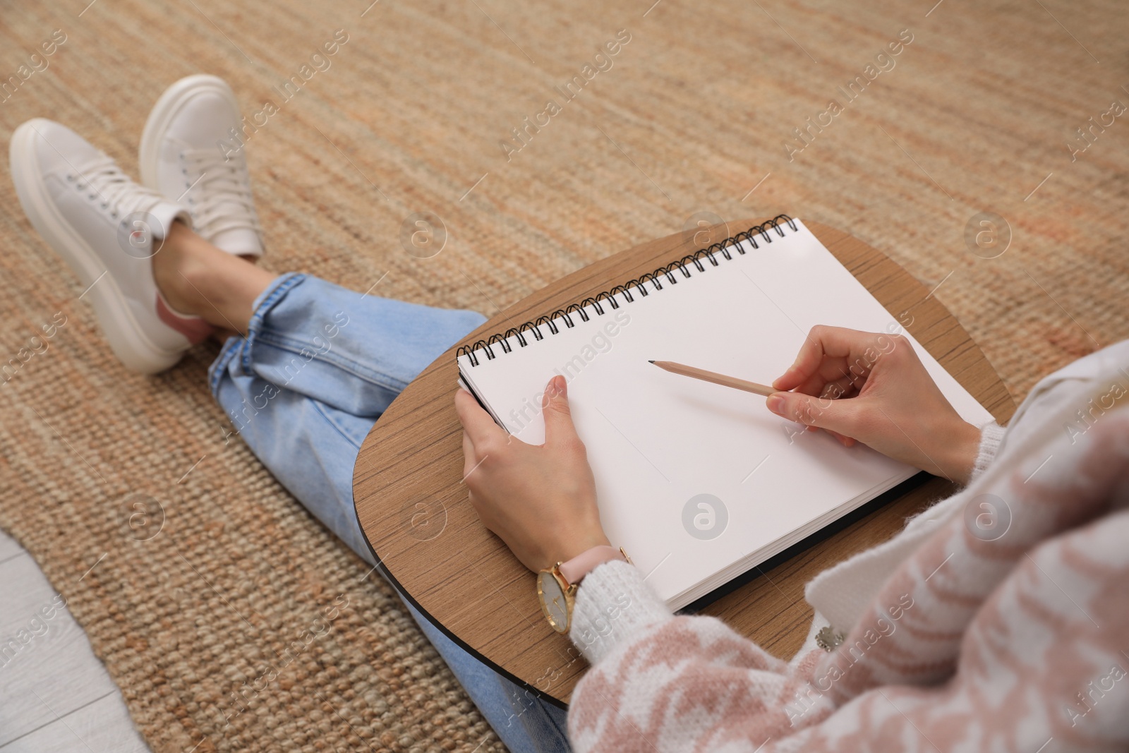 Photo of Woman drawing in sketchbook with pencil on floor at home, closeup