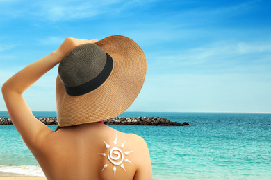 Image of Young woman with sun protection cream on her back at beach, space for text