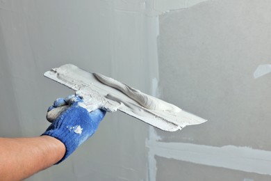 Professional worker holding putty knife with plaster indoors, closeup