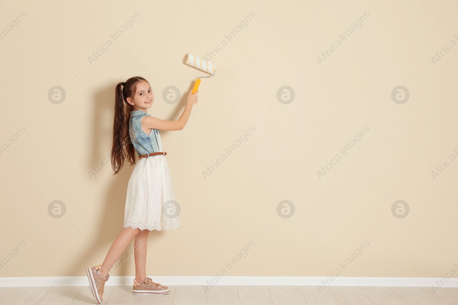 Photo of Child painting color wall with roller brush. Space for text