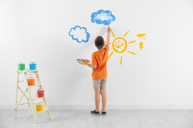 Photo of Little child painting cloud on white wall in room