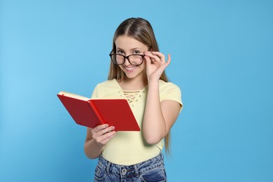 Photo of Teenage girl in eyeglasses reading book on light blue background