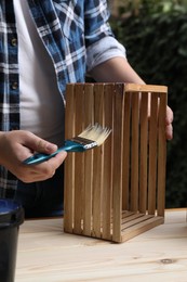 Man applying varnish onto wooden crate at table outdoors, closeup