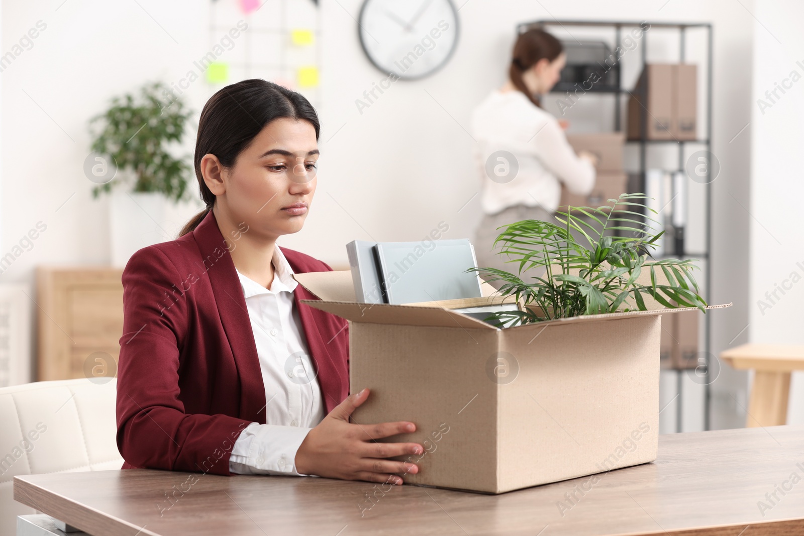 Photo of Unemployment problem. Frustrated woman with box of personal belongings at table in office