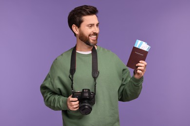 Smiling man with passport, camera and tickets on purple background