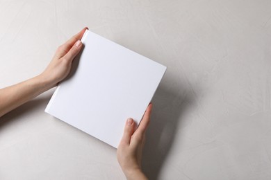 Woman holding book with blank cover at white table, top view. Mockup for design