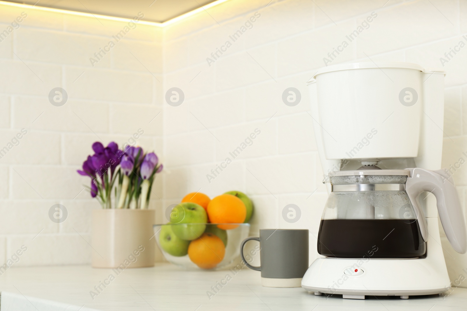 Photo of Coffeemaker, cup, fruits and flowers on counter in kitchen