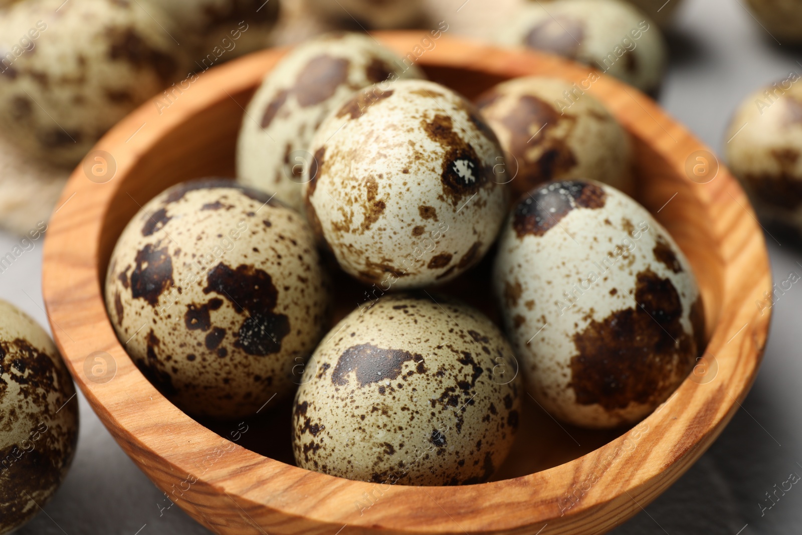 Photo of Wooden bowl and many speckled quail eggs on table, closeup