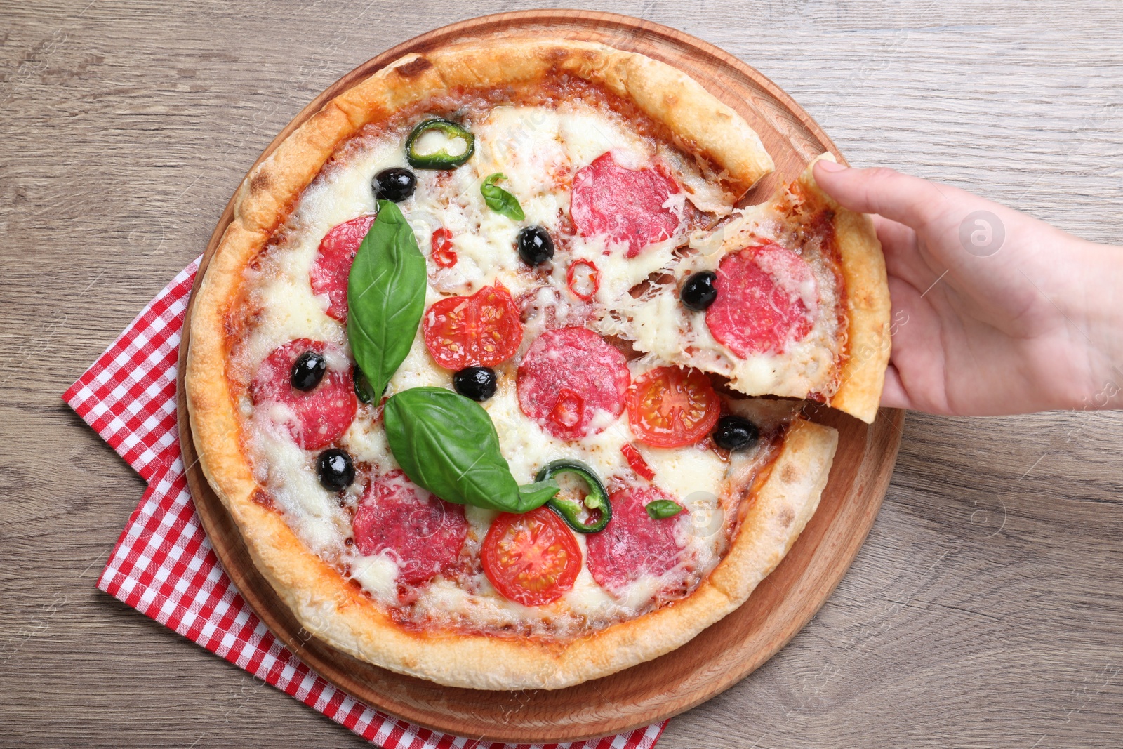 Photo of Woman taking piece of delicious pizza Diablo at wooden table, closeup