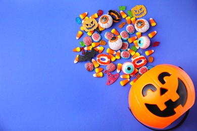 Halloween trick or treat bucket and different sweets on blue background, flat lay. Space for text