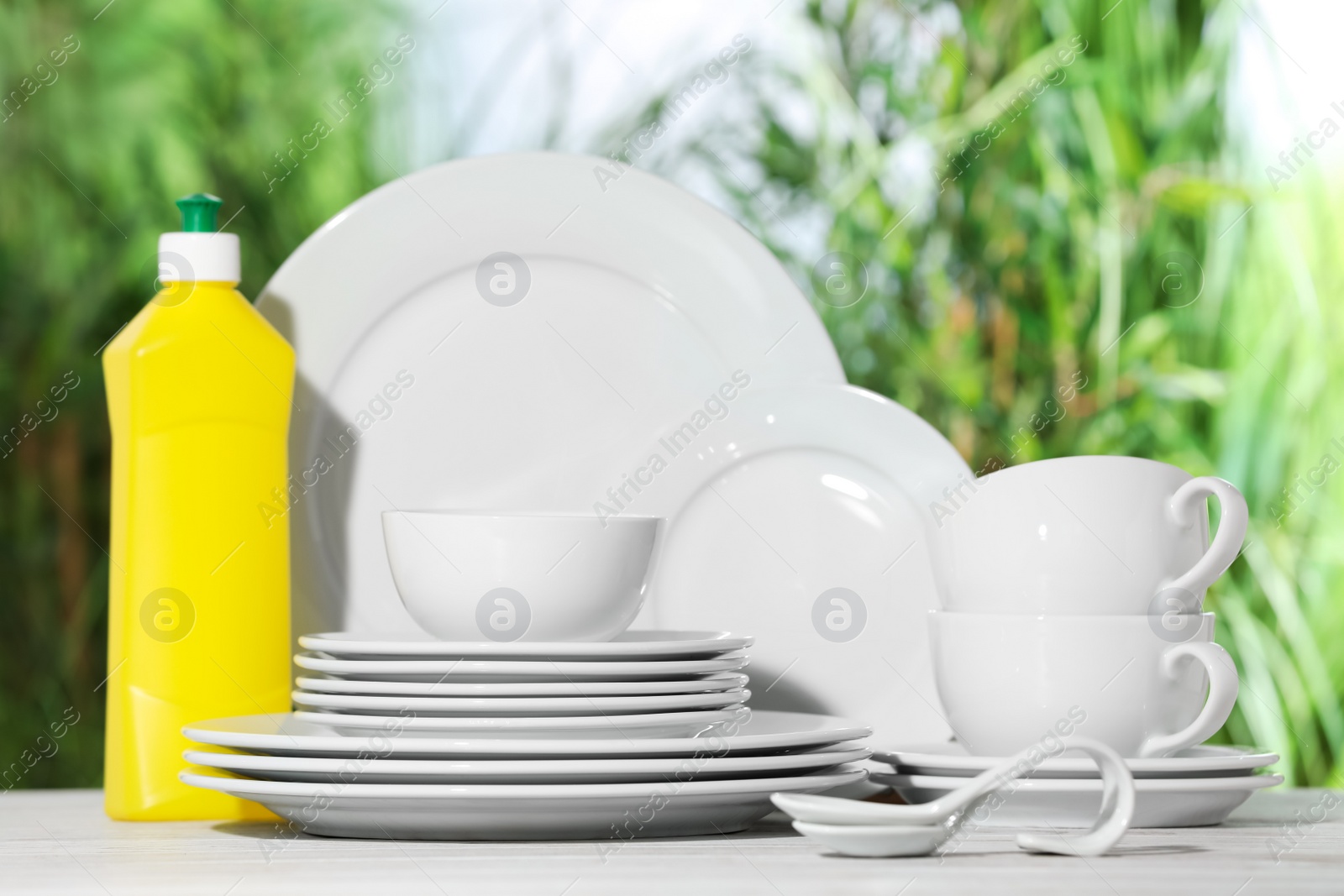 Photo of Set of clean dishware and detergent on white table against blurred background