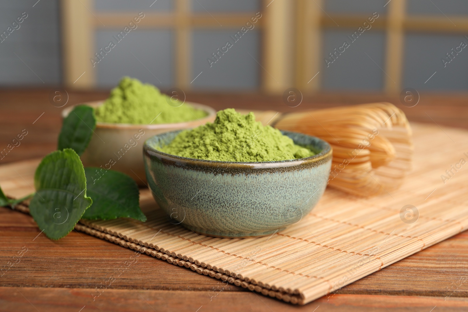 Photo of Green matcha powder and bamboo whisk on wooden table indoors, closeup