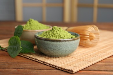 Photo of Green matcha powder and bamboo whisk on wooden table indoors, closeup