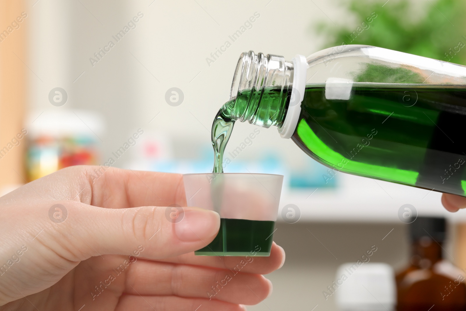 Photo of Woman pouring syrup from bottle into measuring cup against blurred background, closeup. Cold medicine