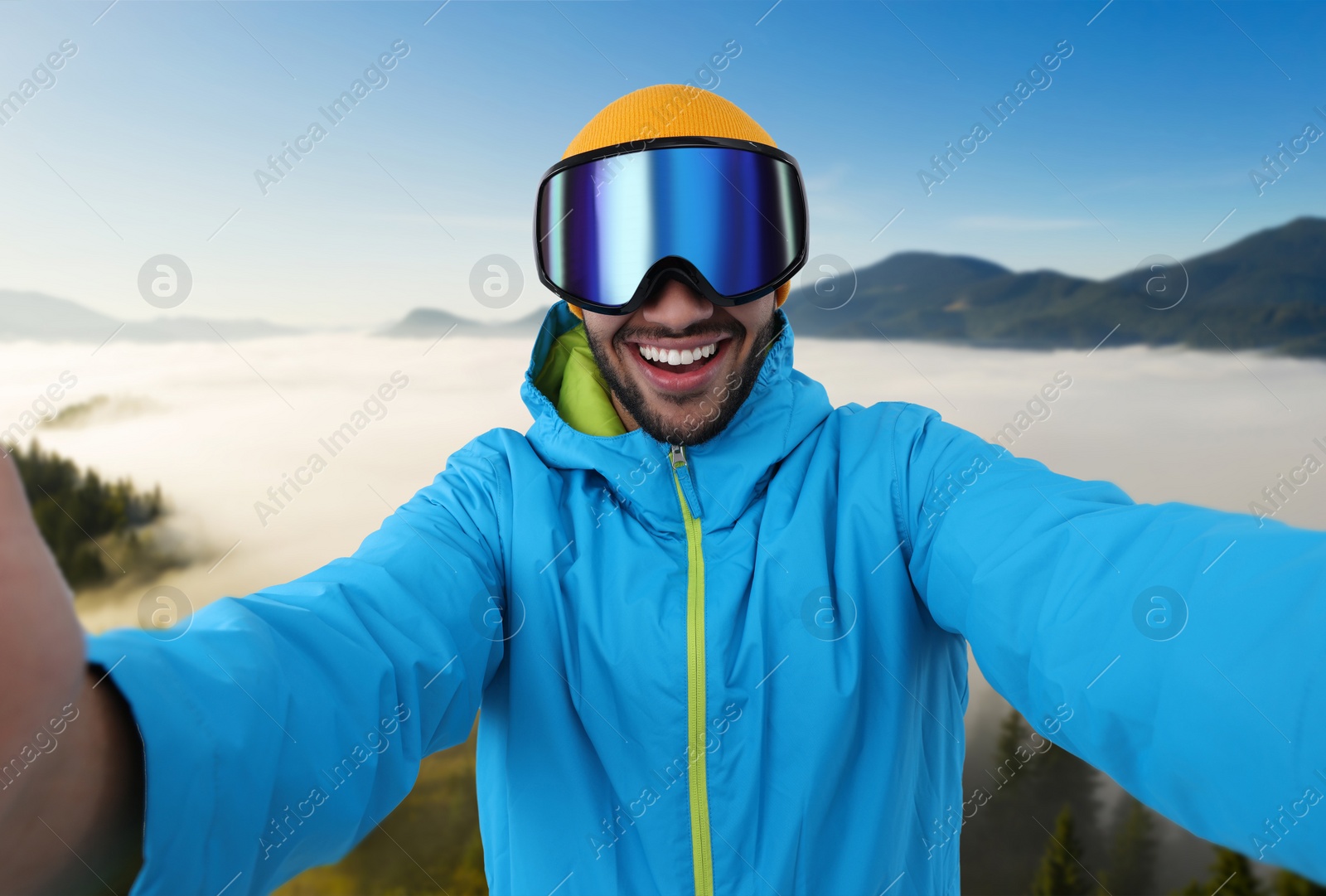 Image of Smiling young man in ski goggles taking selfie in mountains