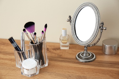 Photo of Organizer with cosmetic products for makeup and mirror on table against light wall